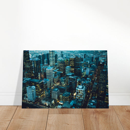 Aerial cityscape of illuminated buildings at twilight with a dusky sky backdrop.