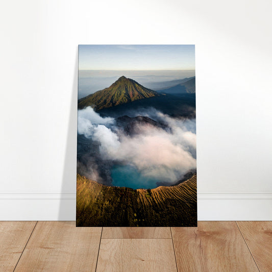 Aerial view of an active volcano with smoke rising from the crater, surrounded by green mountain slopes and a blue crater lake under morning light.
