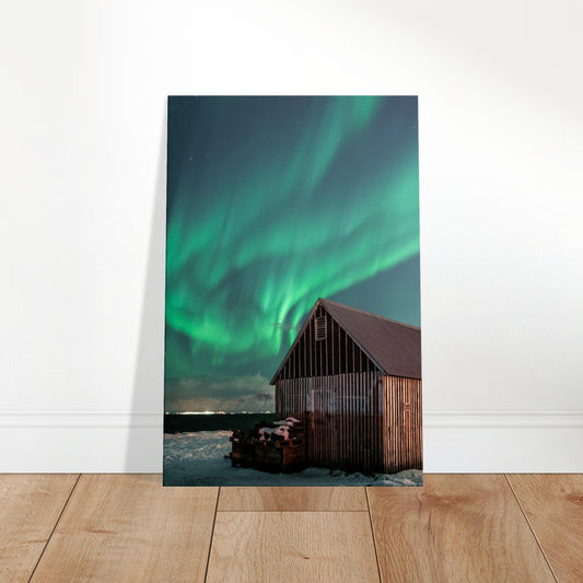 Wooden hut in snowy landscape under vivid green aurora borealis and a starry night sky.